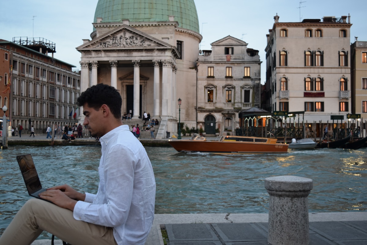 A man sitting on a ledge using a laptop outdoors