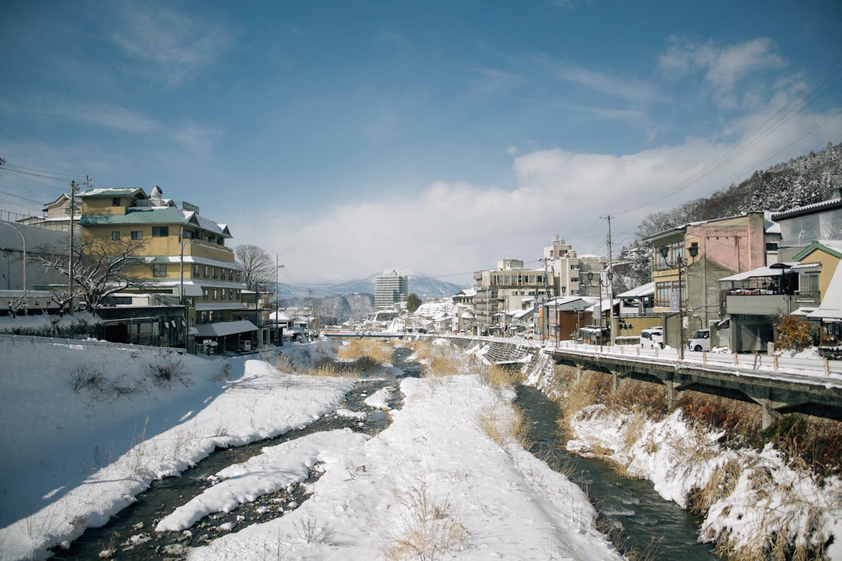 A river running through a snow-covered Japanese town with traditional buildings
