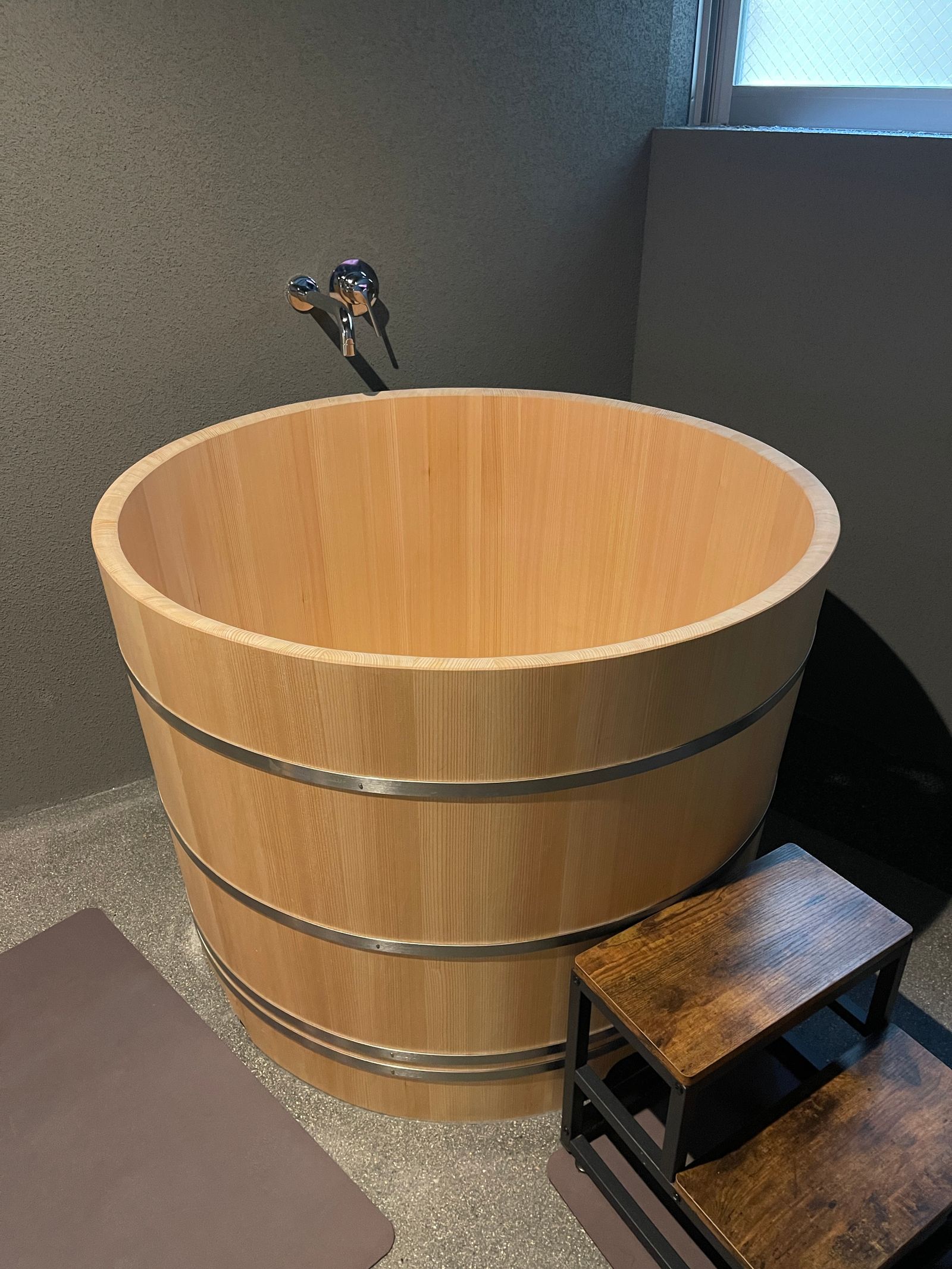 Deep hinoki-wood Japanese soaking tub with a washing stool beside it